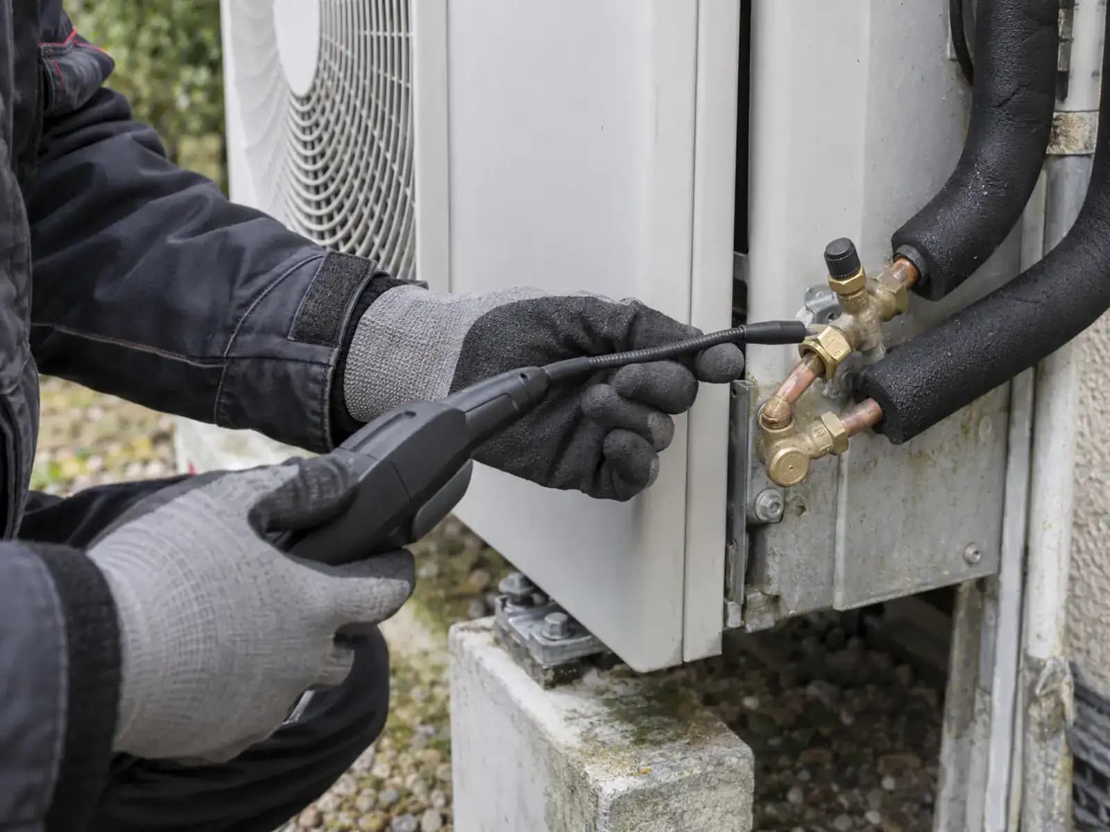 Mains gantées approchant la sonde d'un détecteur de fuite électronique des raccords d'une unité extérieure