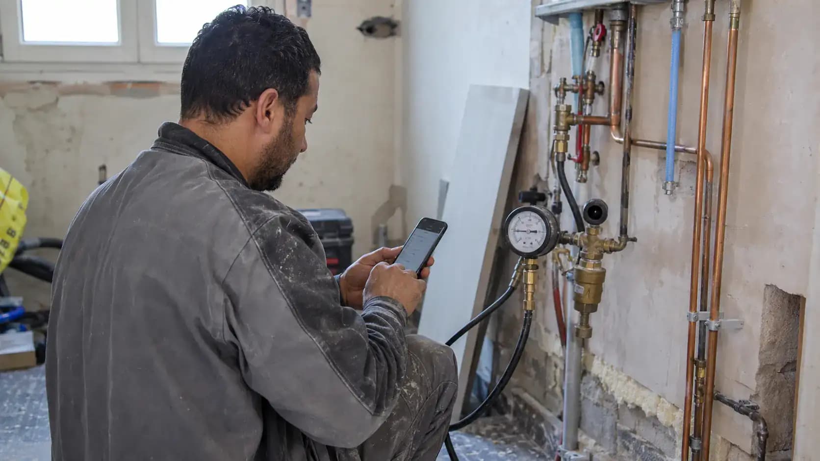 Artisan relevant un manomètre, téléphone en main, pendant une intervention